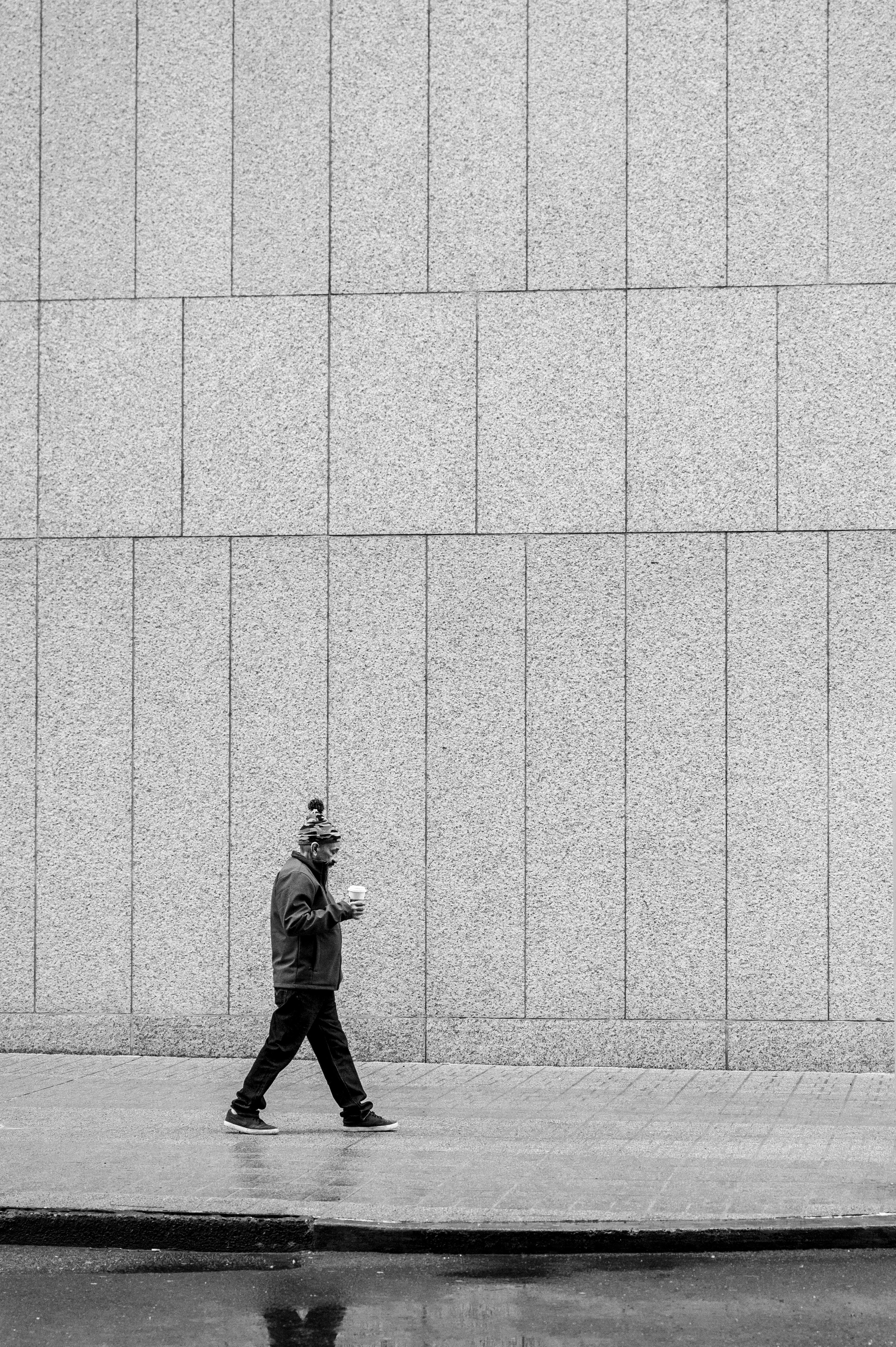 Man walking with coffee by a blank wall in Portland. Black and white street photography.