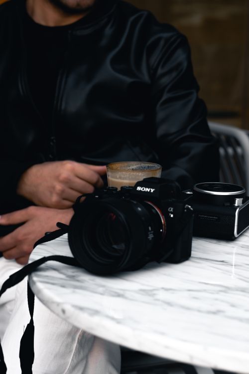 Free A man in a leather jacket drinks coffee at a café in Ankara with a camera on the table. Stock Photo