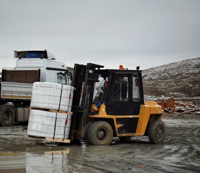 Forklift transporting large pallet in an outdoor industrial setting.