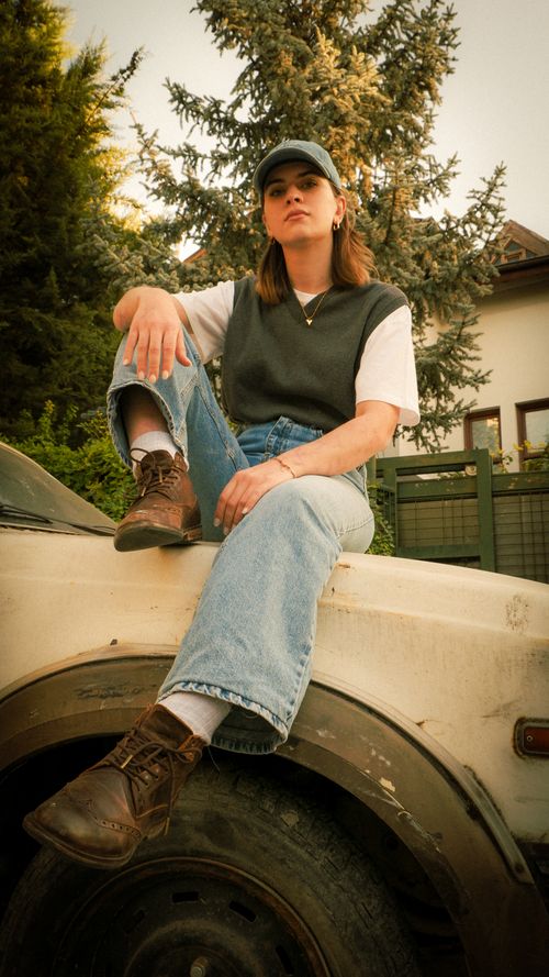 Free A young woman in casual attire sits confidently on a vintage car outdoors. Stock Photo