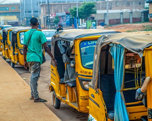 Free A man walks by yellow rickshaws lined up on a street in Lagos, Nigeria, showcasing urban life. Stock Photo