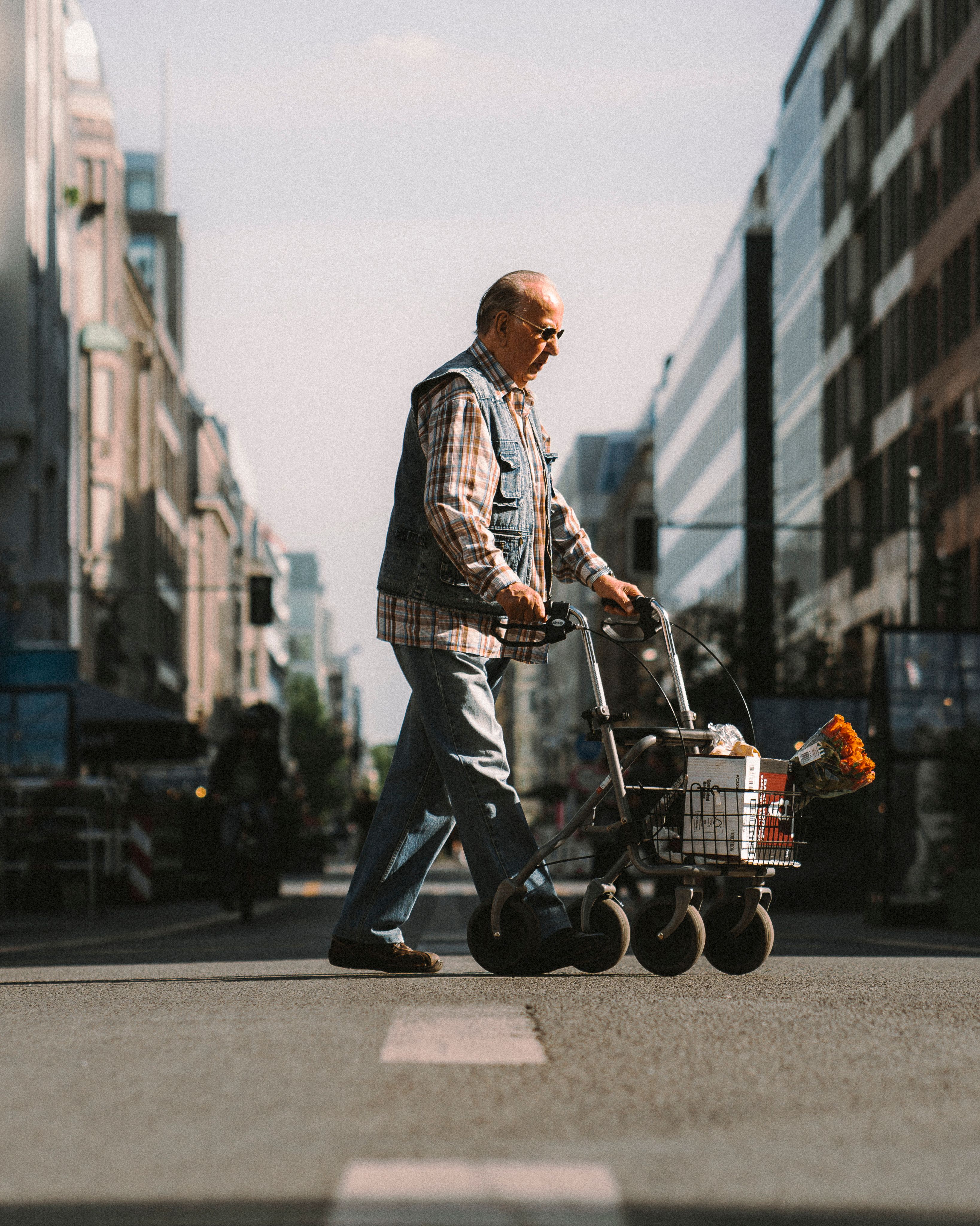 An elderly man crossing a Berlin street with a walker and groceries, underlining urban life and independence.