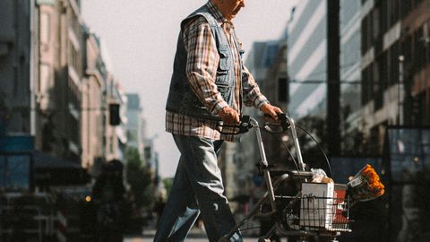 An elderly man crossing a Berlin street with a walker and groceries, underlining urban life and independence.