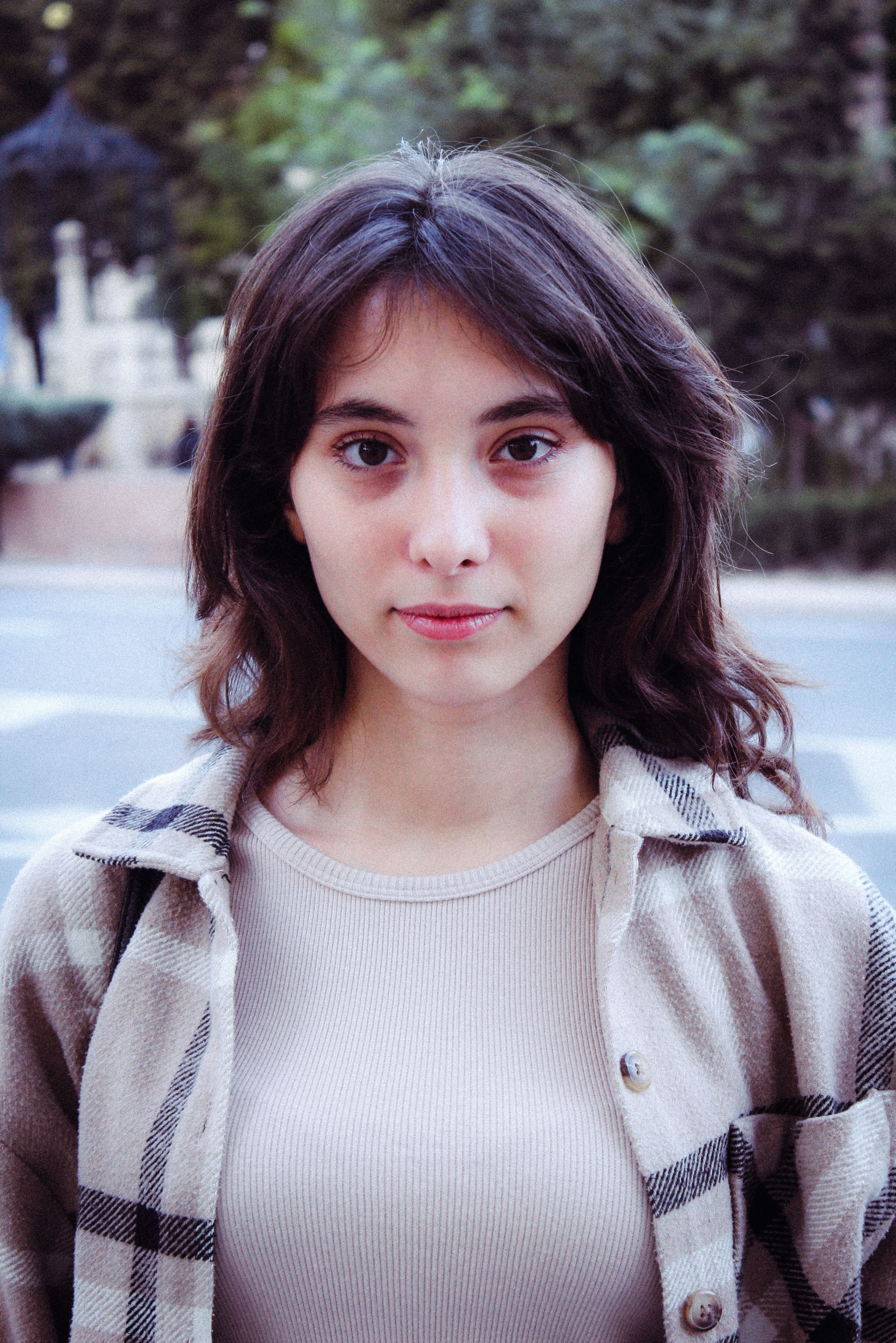 Portrait of a young woman with a neutral expression in an urban environment.