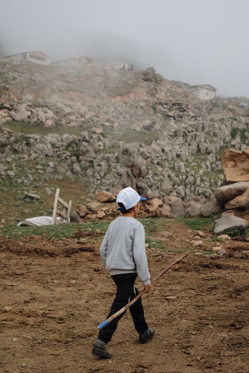 Free A child in a cap walks with a stick in a rural, rocky village setting. Stock Photo