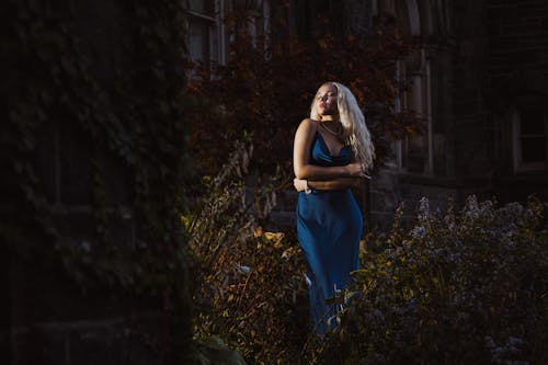 Blonde Model in Blue Dress Standing behind Bush