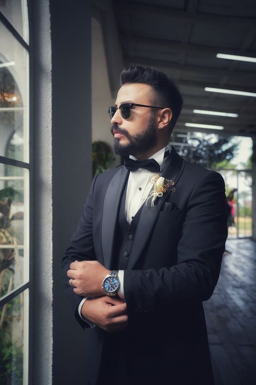 Free Elegant groom in a black suit and sunglasses, standing indoors, showcasing wedding fashion. Stock Photo
