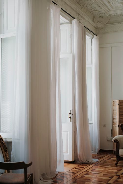 Free Bright vintage interior featuring tall white curtains and intricate ceiling details in a classic room. Stock Photo