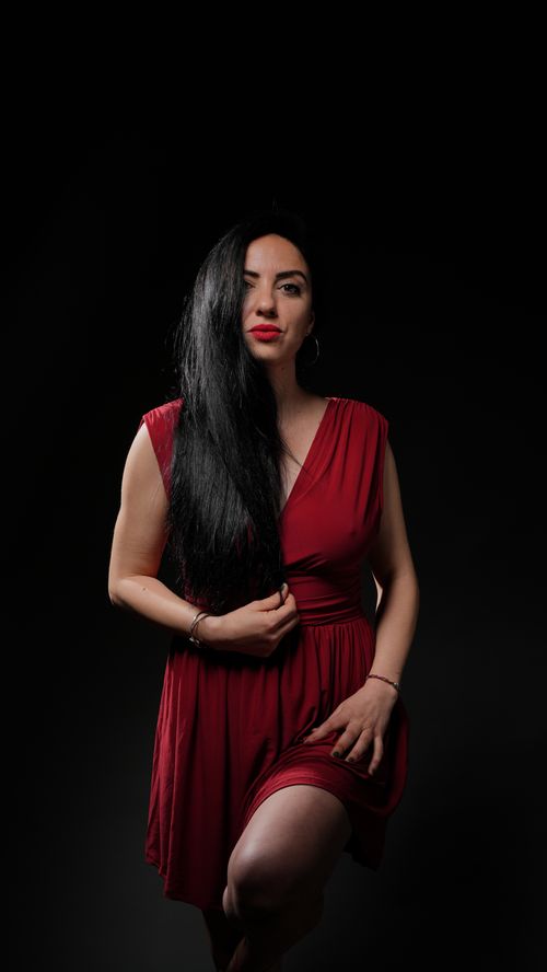 Free Portrait of a woman in a stylish red dress with striking contrast on black background. Stock Photo