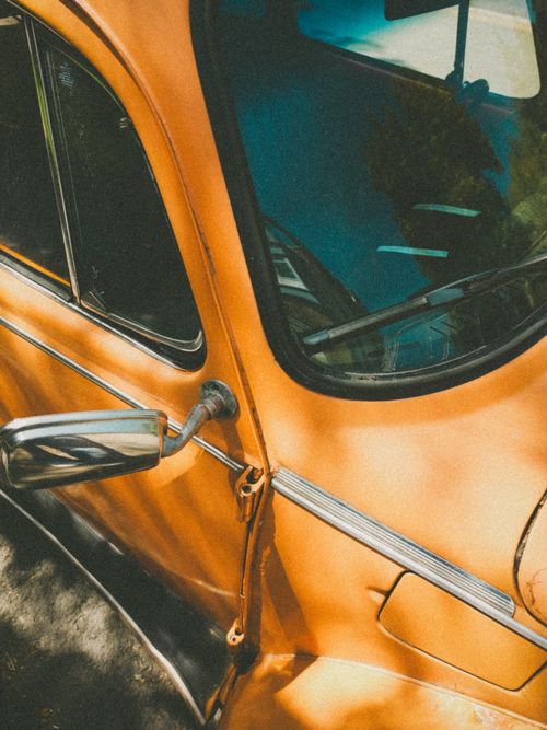 Free Close-up of a vintage orange car with a retro feel, showcasing window and side mirror details. Stock Photo