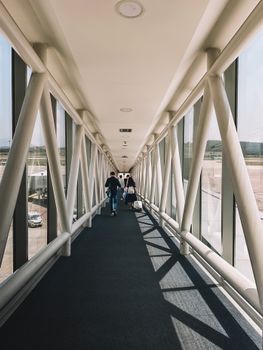 People walking in a glass airport corridor with a diminishing perspective.