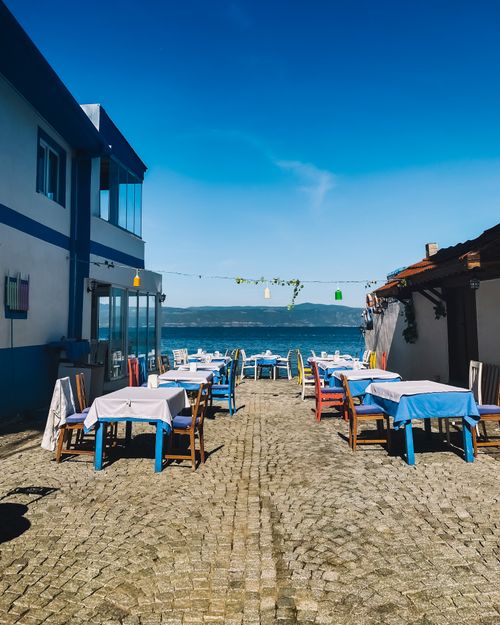 Free Outdoor dining scene by the sea in Mudanya, Türkiye, featuring vibrant tables and a clear blue sky. Stock Photo