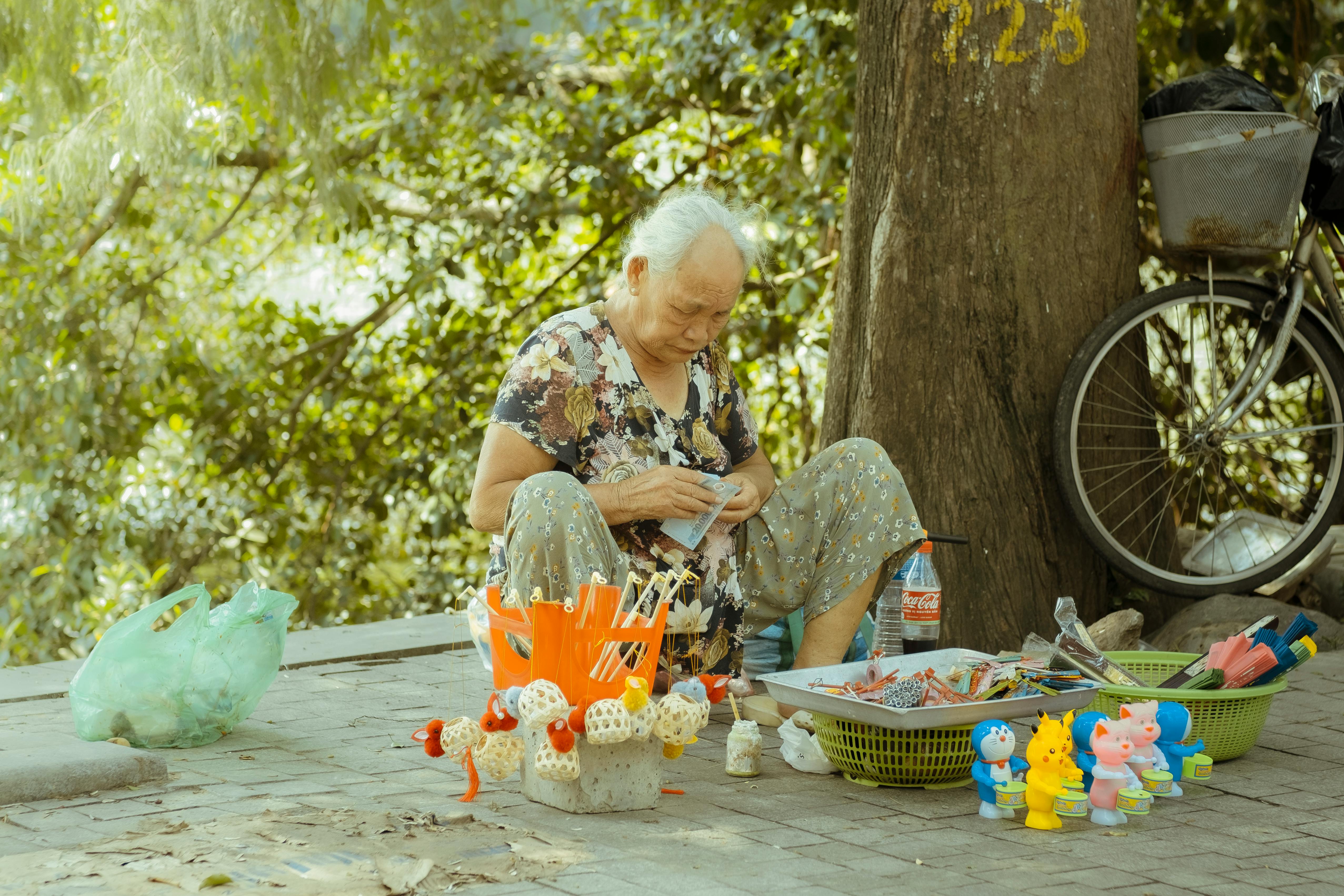 elderly woman selling toys under a tree