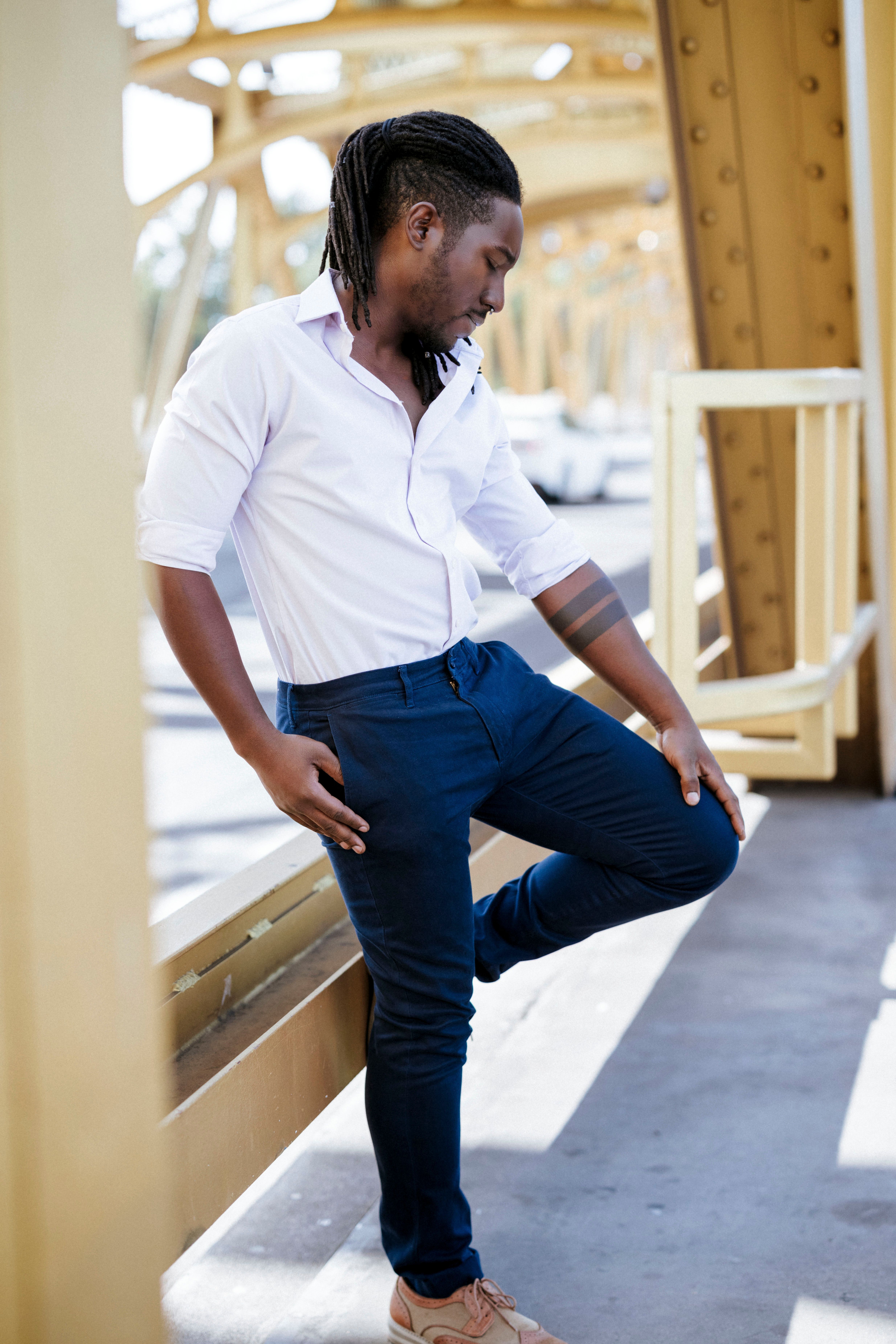 A fashionable man leans casually on a metallic bridge in daylight.