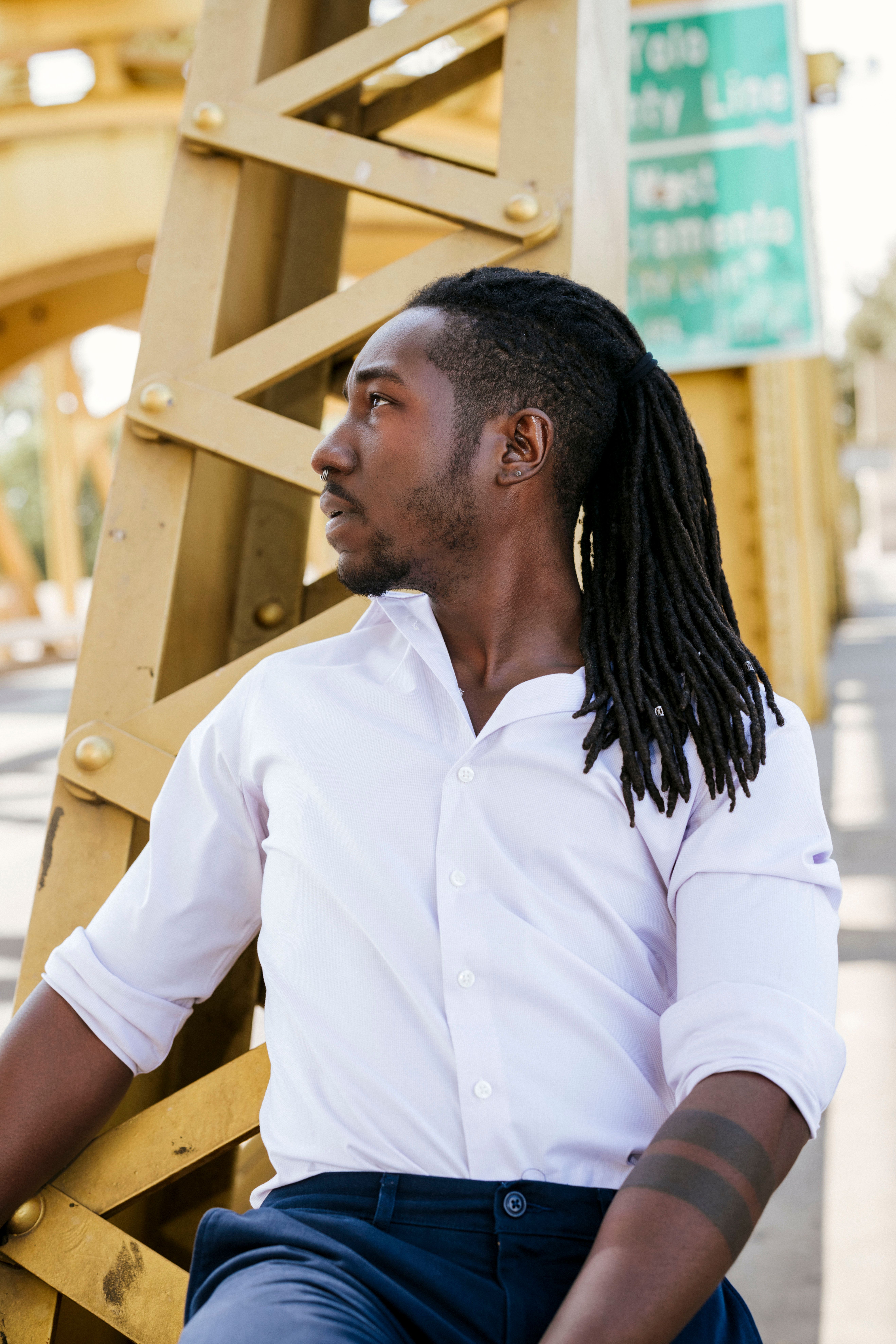 African American man with dreadlocks leaning on bridge in city. Urban fashion and architecture.