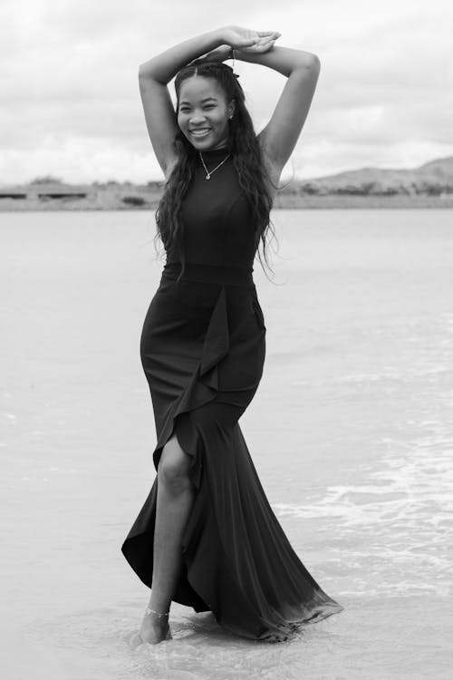 Free Smiling Model in Black Dress on Sea Shore in Black and White Stock Photo