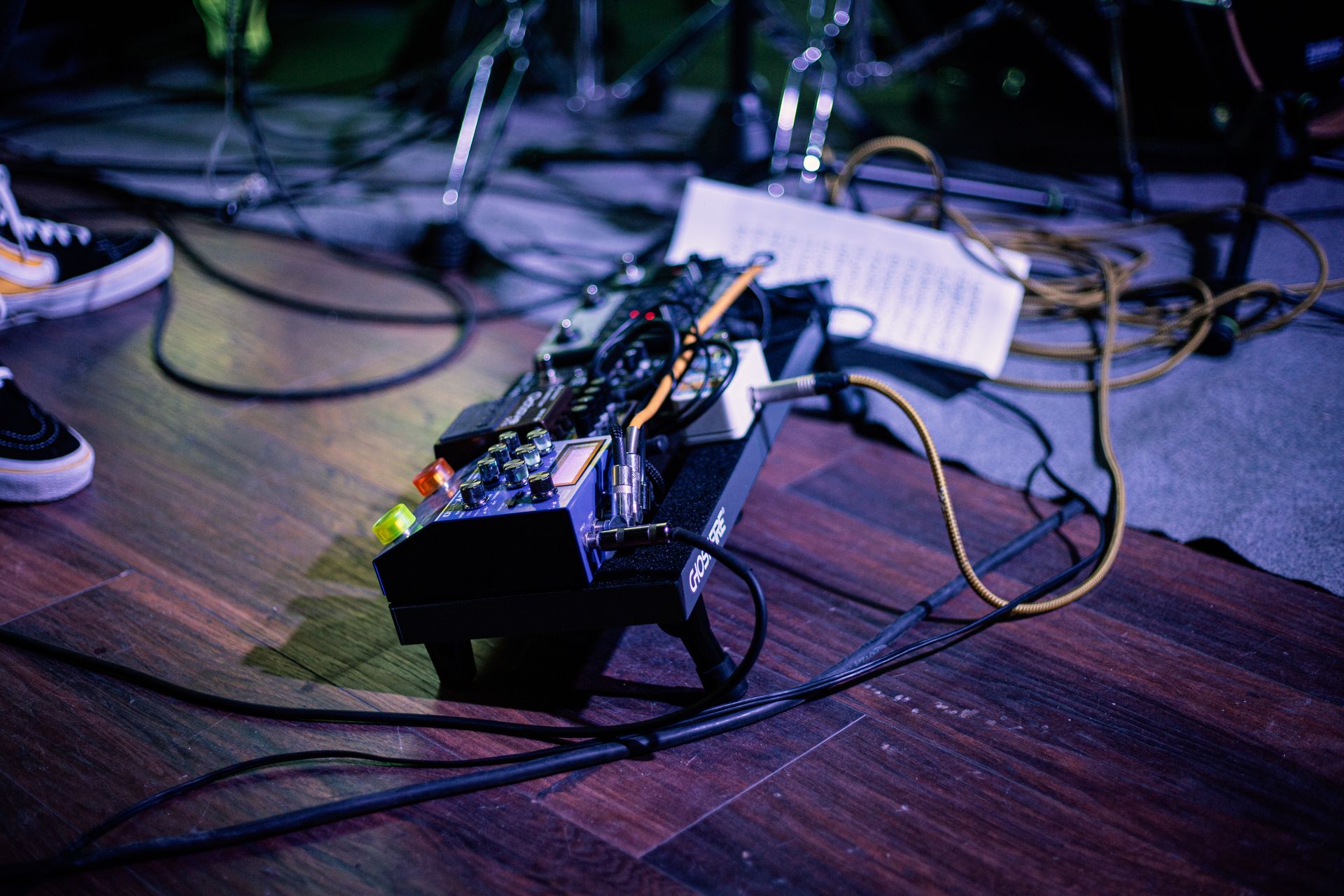 Detailed view of a music pedalboard with cables and equipment on a stage.