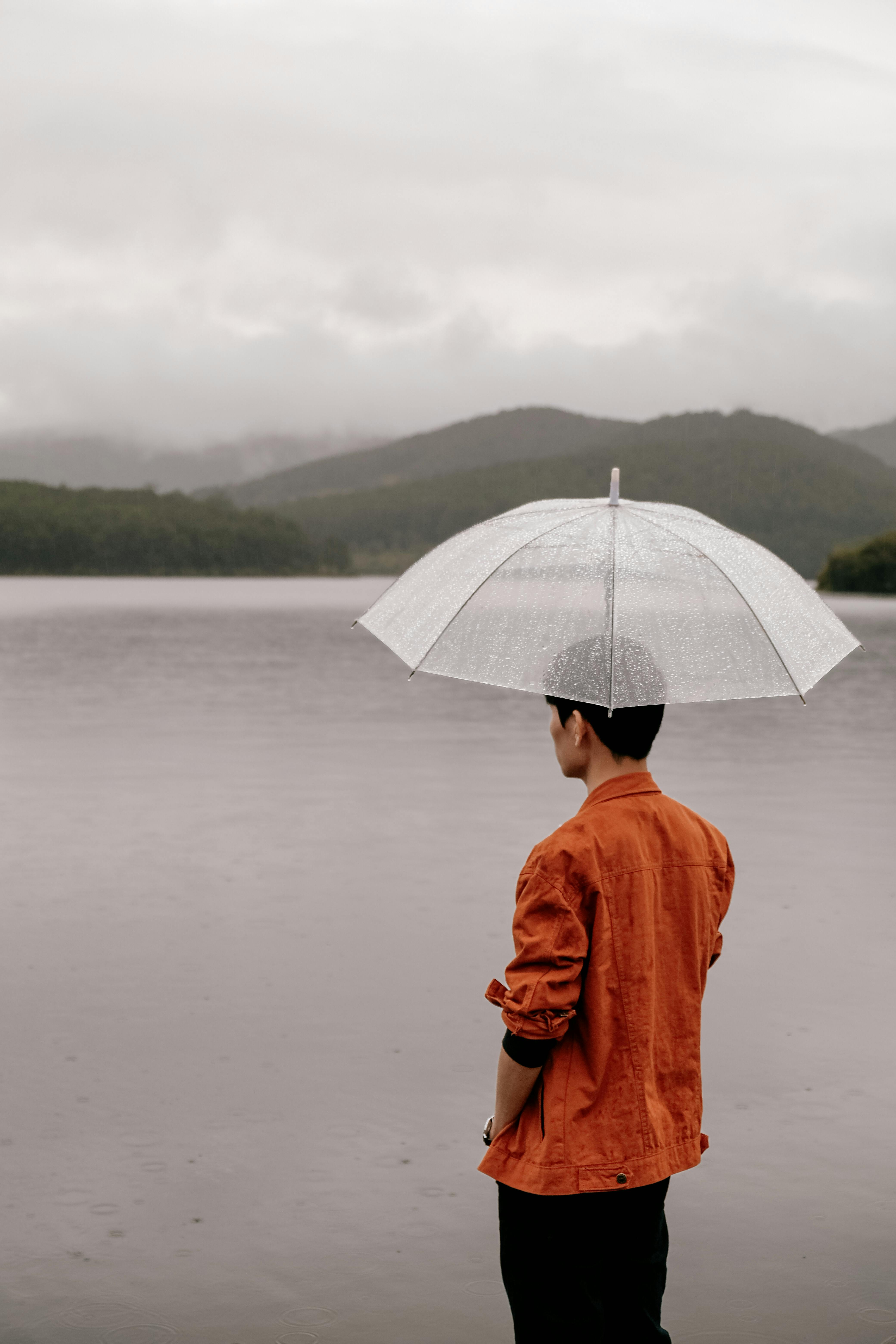 Man standing by Dalat lake under an umbrella on a rainy day, Vietnam.