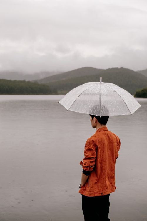 Free Man standing by Dalat lake under an umbrella on a rainy day, Vietnam. Stock Photo
