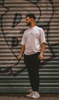 Young man in casual sportswear standing by urban graffiti, showcasing street style fashion.