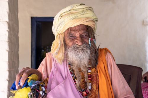 Free An elderly man with a colorful turban and beads smiling warmly in a traditional setting. Stock Photo