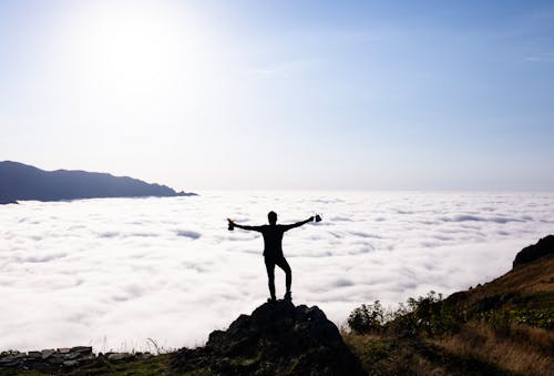Man Standing on Rocks on Hilltop over White Cloud