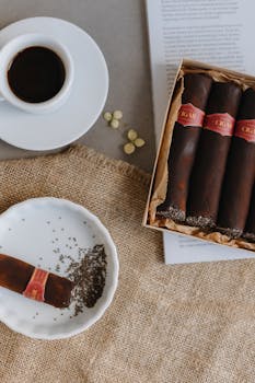 Aesthetic flat lay of cigars, coffee, and pages on rustic fabric.