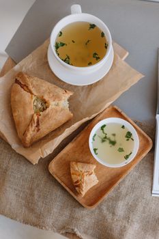 Flat lay of a cup of soup and a pastry on a rustic table setting with decorative garnishing.