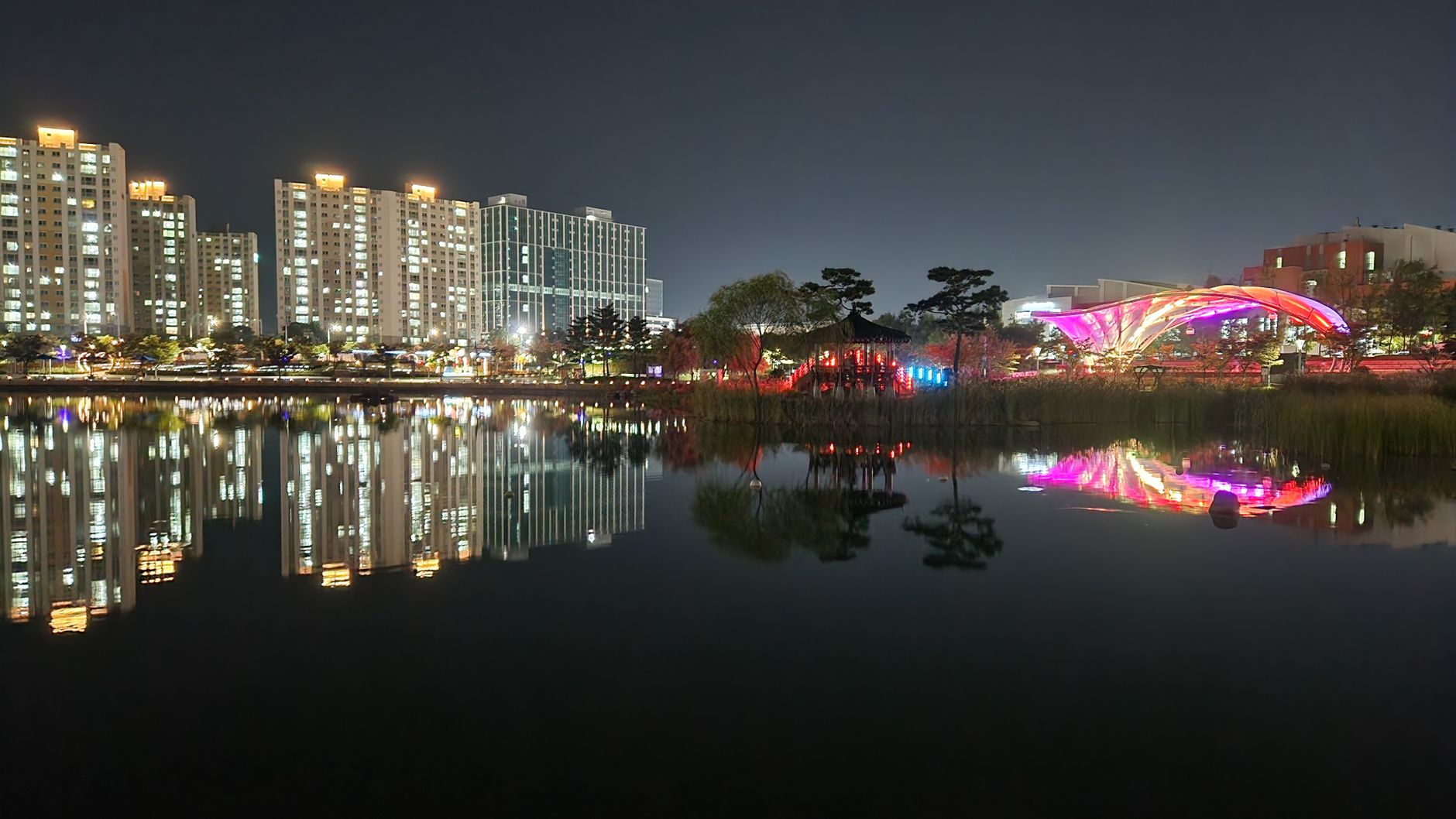 Illuminated buildings and colorful reflections in a serene lake park at night.