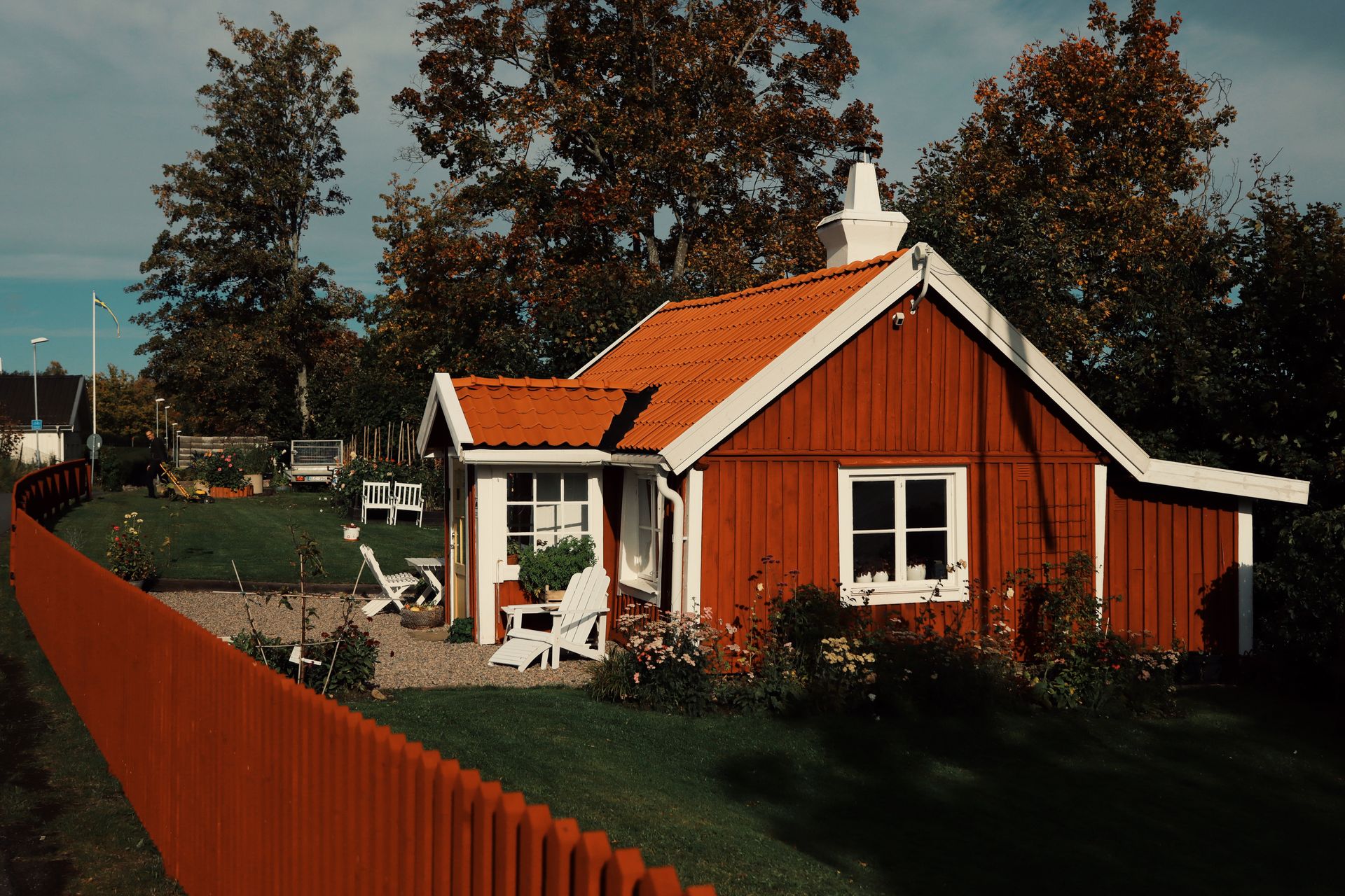 Picturesque red wooden cottage with white trim in a summer village setting, surrounded by greenery.
