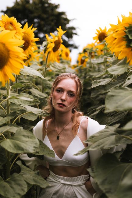 A striking portrait of a young woman standing among blooming sunflowers in summer.