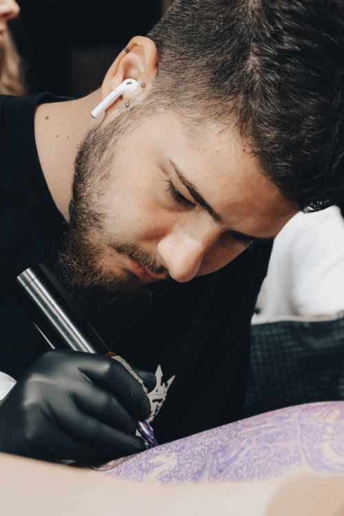 Free Tattoo artist with earpod intently works on client's design in studio. Stock Photo