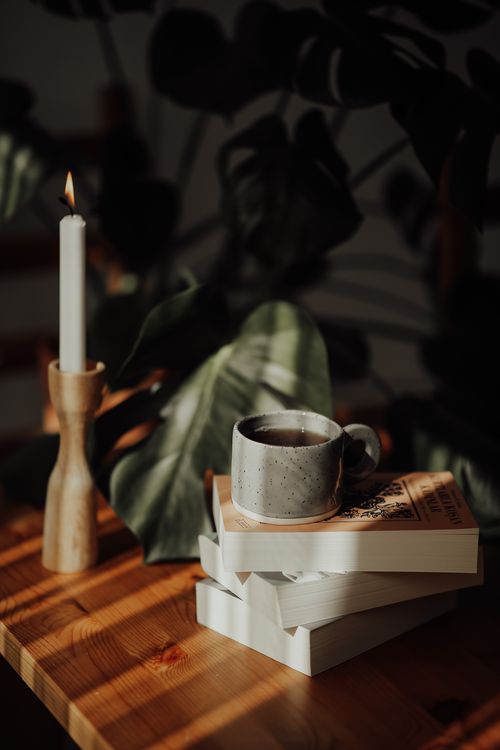 Free Warm, inviting scene with coffee, books, candle, and monstera leaves. Stock Photo