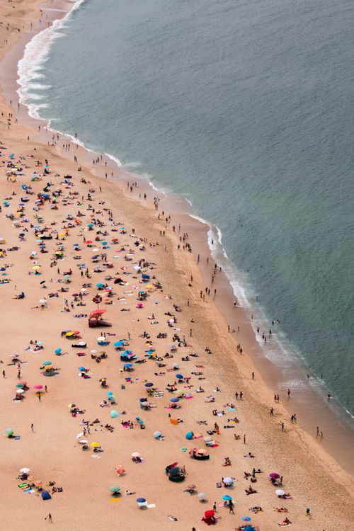 Free A vibrant aerial capture of Nazaré Beach, Portugal, bustling with sunbathers and colorful umbrellas. Stock Photo