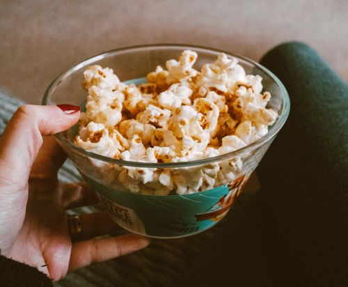 Free Close-up of a hand holding a glass bowl filled with delicious popcorn. Perfect snack time capture. Stock Photo