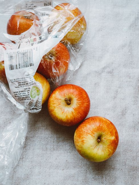 Freshly picked red apples with a few in plastic packaging on a neutral fabric surface.