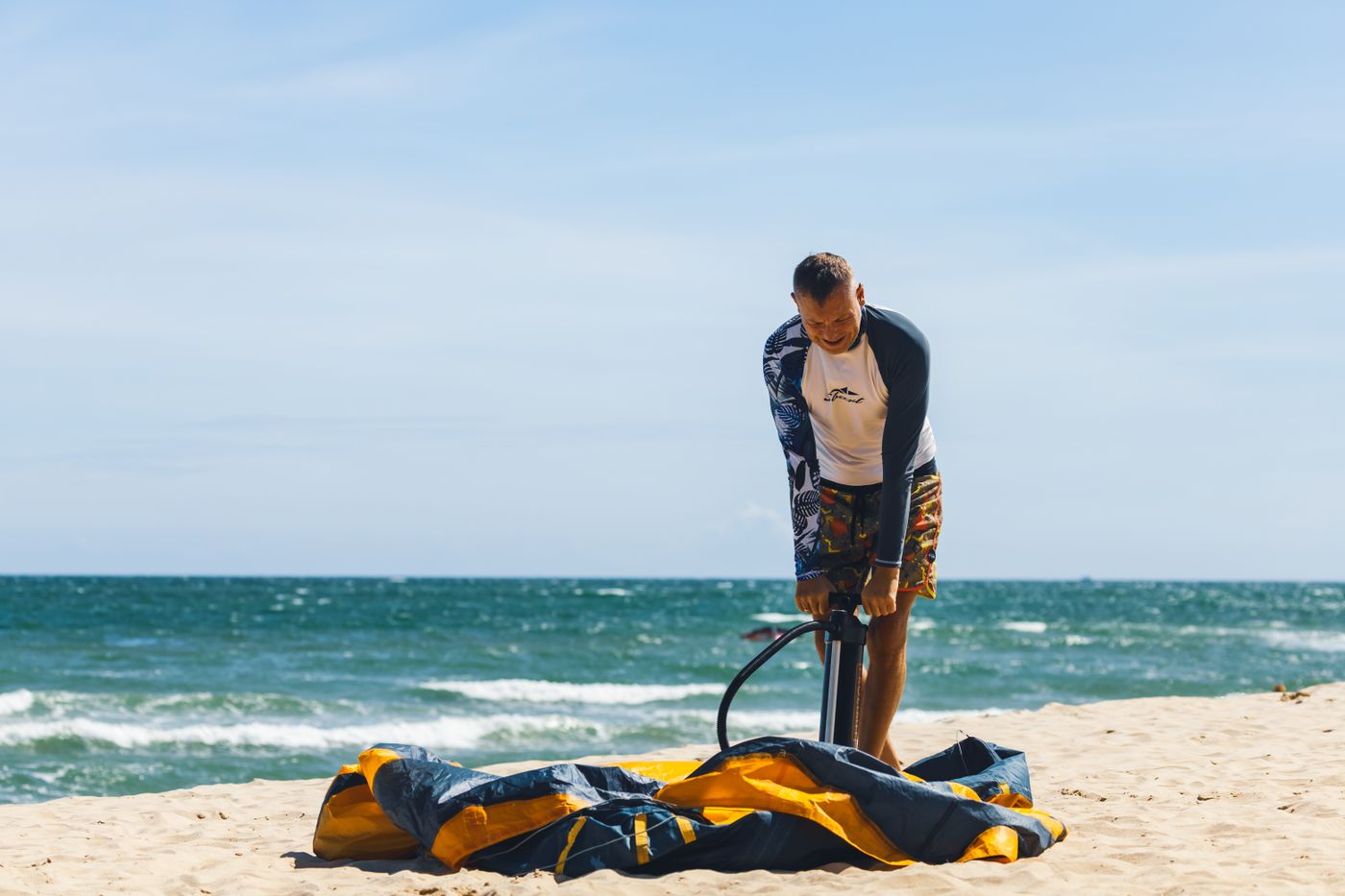 Man inflating a stand-up paddle board on a sandy beach