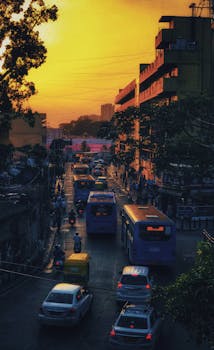 Cars and buses navigate through busy city streets under a vibrant sunset sky, capturing urban life.