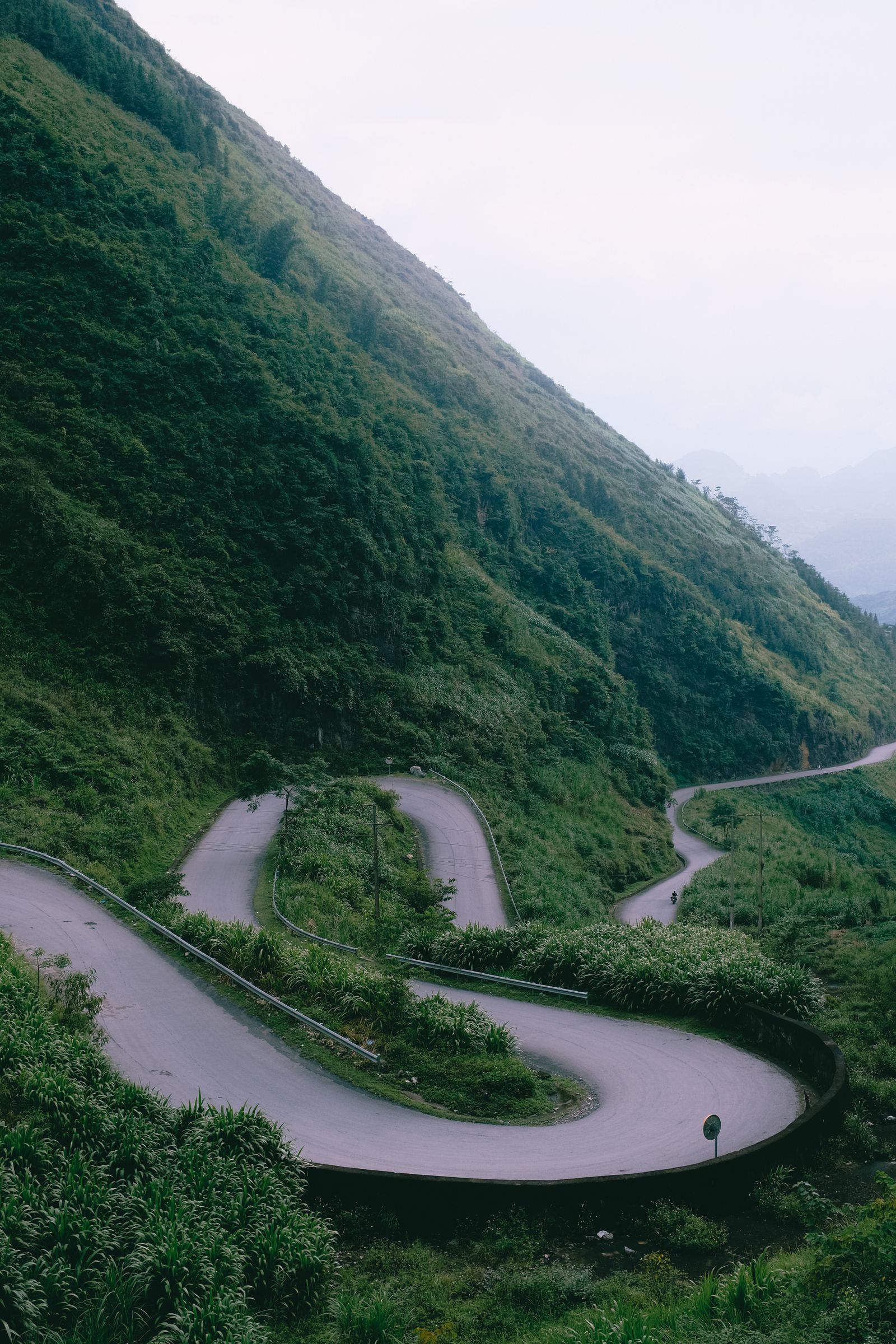 Winding mountain road on the Ha Giang Loop with green slopes and mist