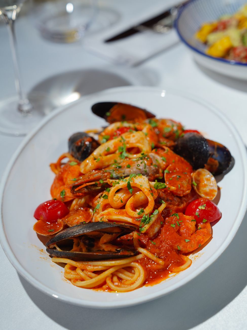 A generous bowl of linguine pasta tossed with plump mussels in a vibrant red arrabbiata sauce, garnished with fresh green parsley and golden grated cheese