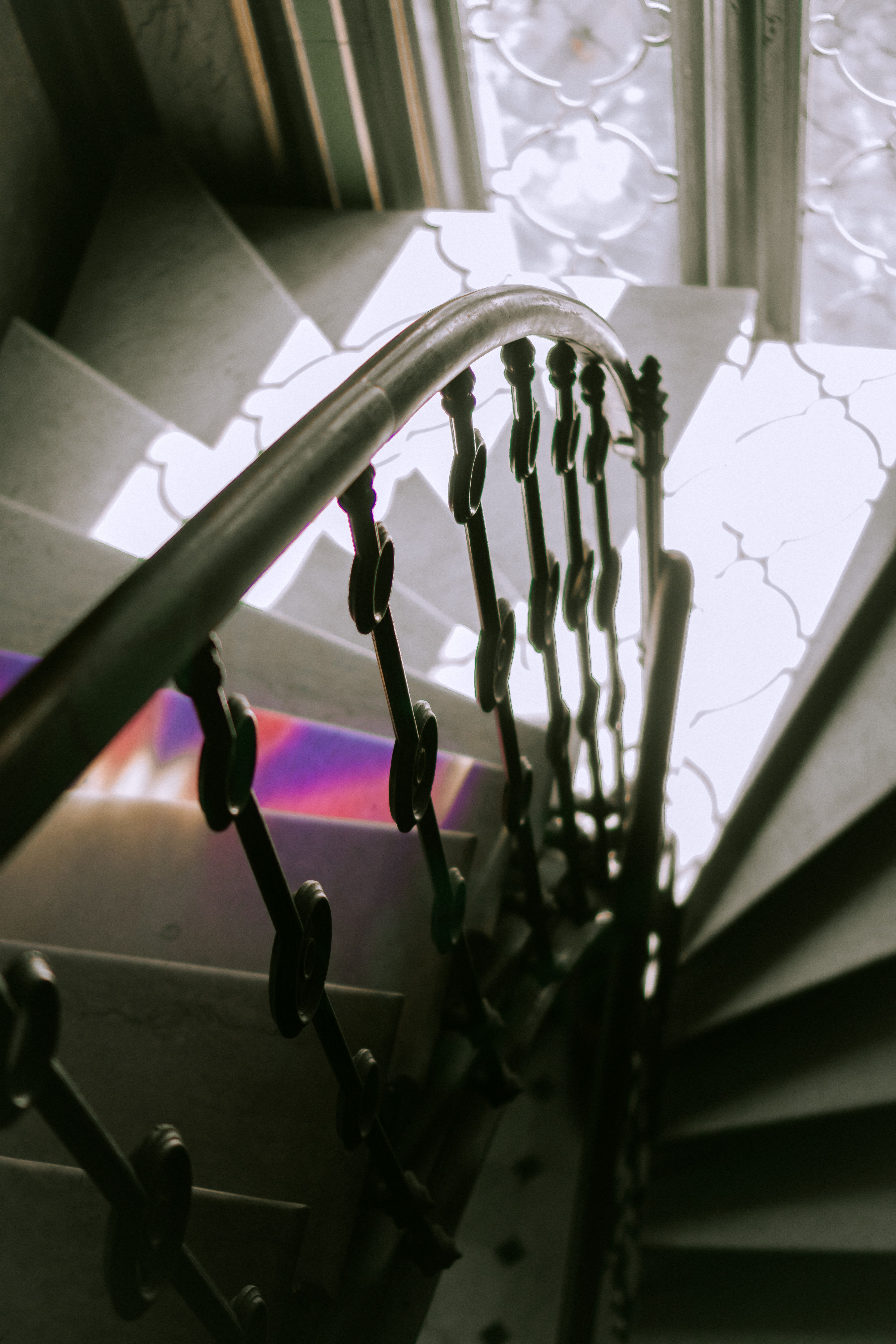 Scară în spirală cu balustradă din fier forjat cu ornamente, sub o lumină difuză