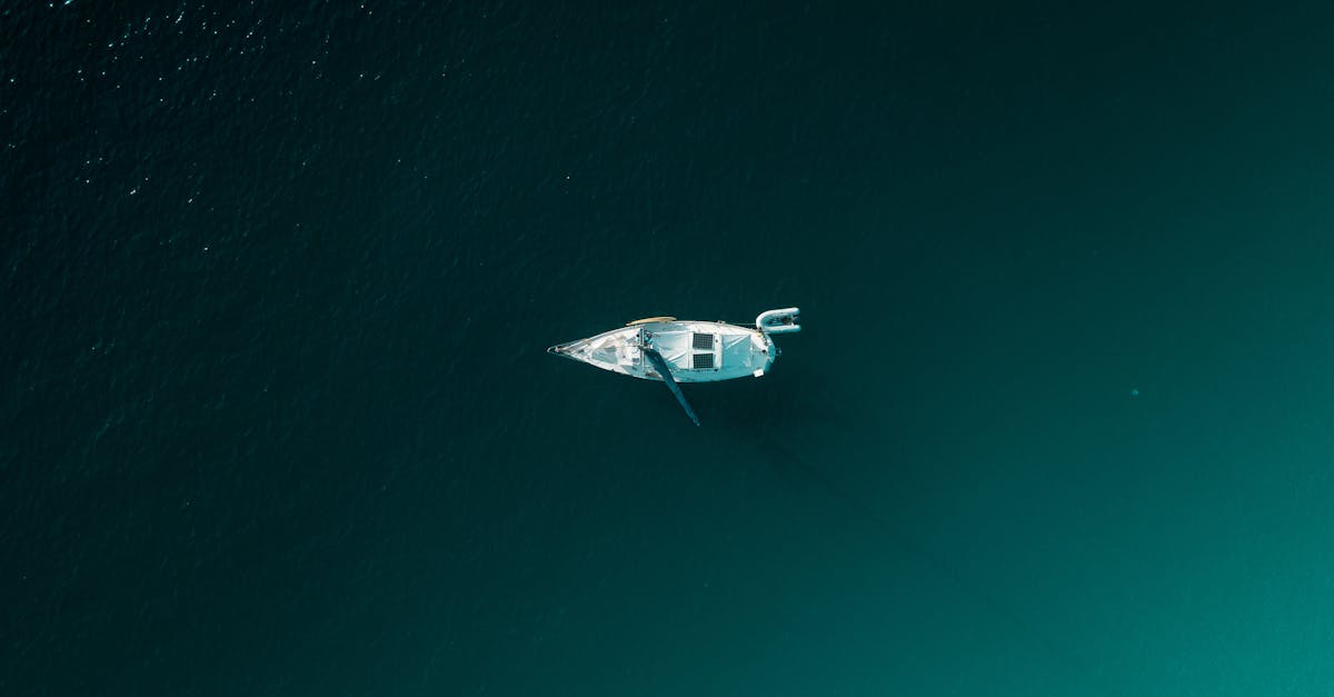 Aerial shot of a sailboat floating on calm, deep-colored water in Thailand, creating a serene and peaceful scene.