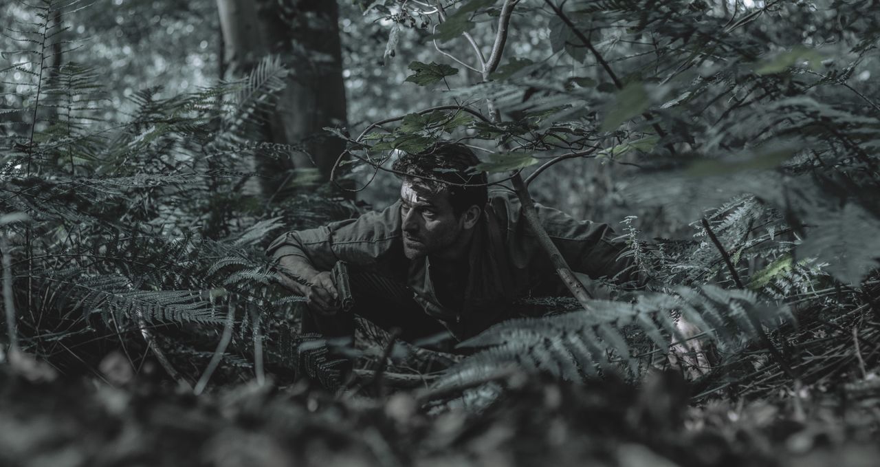 a man crouches in dense forest foliage blending with his surroundings
