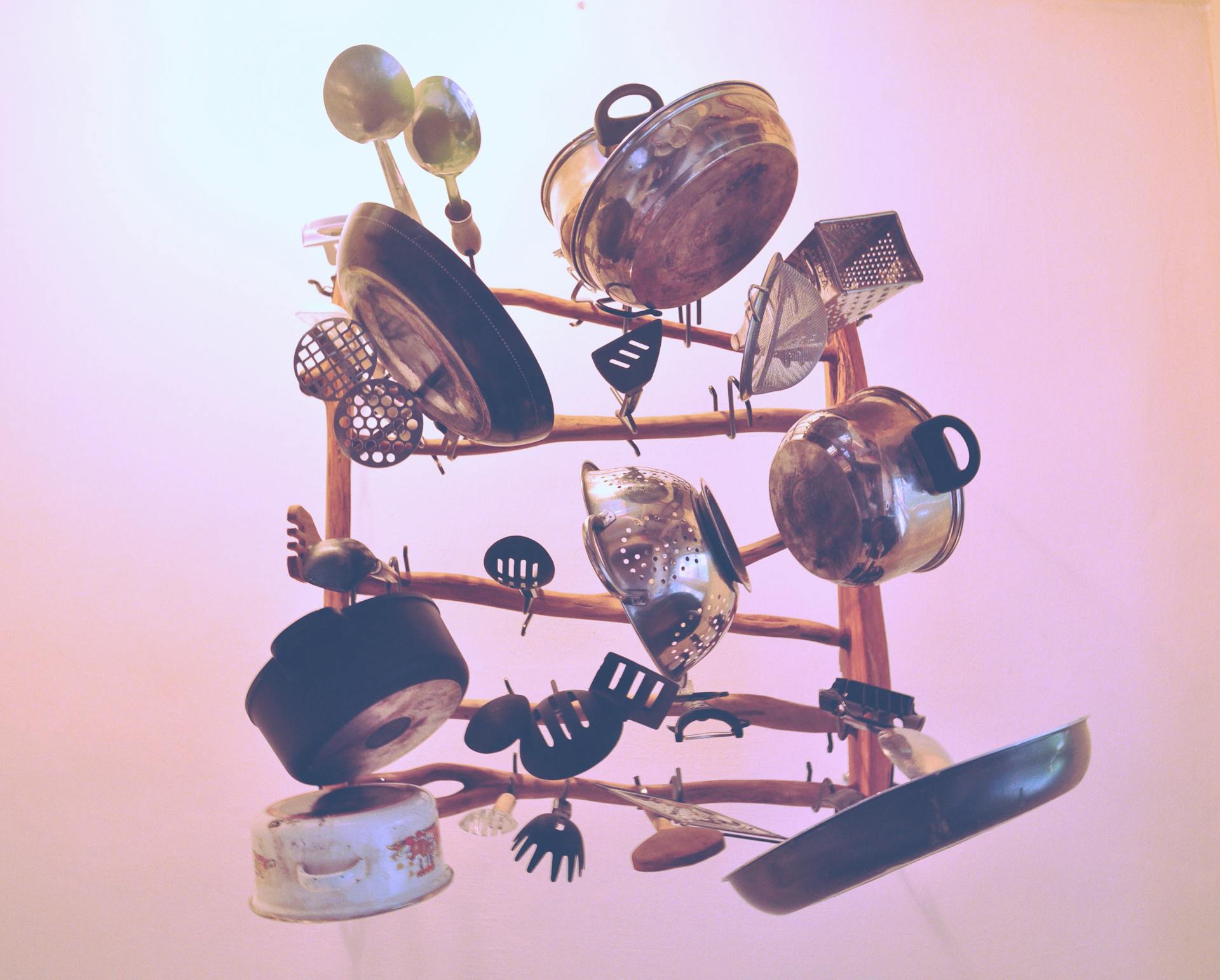 Artistic assortment of hanging kitchen cookware and utensils on a wooden rack indoors.