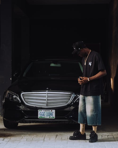 Man Wearing Black T-shirt and Loose Short Jeans Looking at a Mercedes