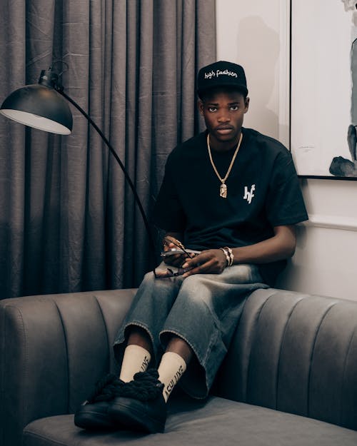 Man in High Fashion T-shirt and Loose Short Jeans Sitting on the Back of the Sofa