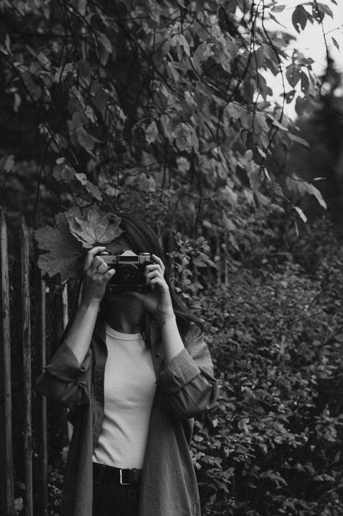Free Artistic black and white portrait of a woman taking pictures in a leafy outdoor setting. Stock Photo