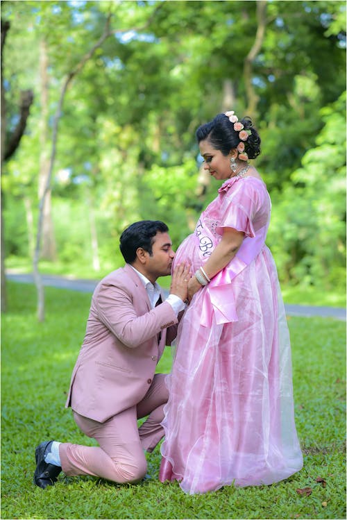 Man Kneeling and Kissing Pregnant Woman in Pink Dress