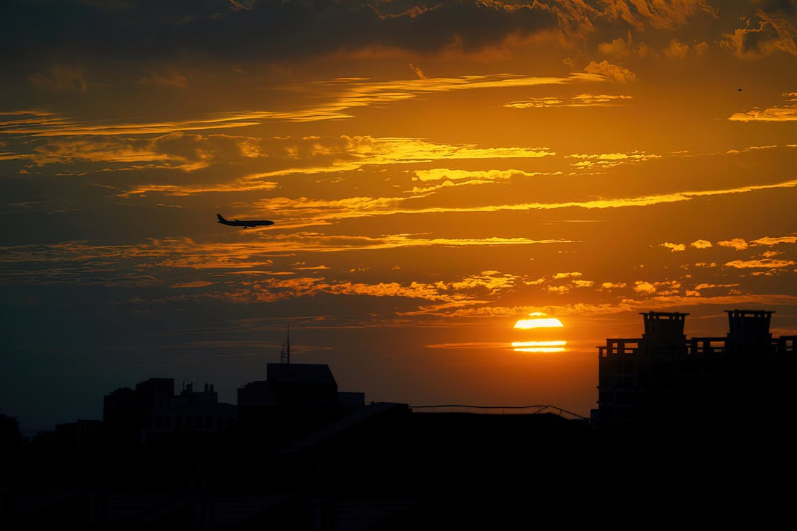 Silhouetted Buildings in City and a Flying Airplane at Sunset