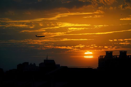 Free A silhouette of buildings and an airplane at sunset with an orange sky. Stock Photo